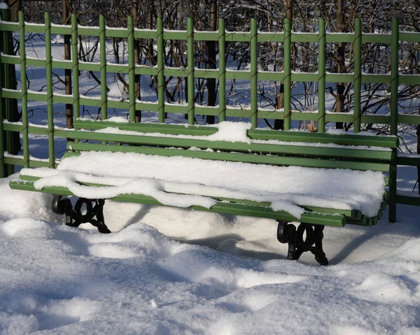 Snow-covered bench in park.