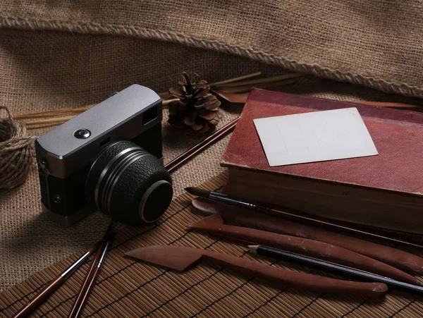 Câmera vintage velha, cartão postal em branco, pincéis de pintura e livro vermelho na juta, saco de linho — Fotografia de Stock