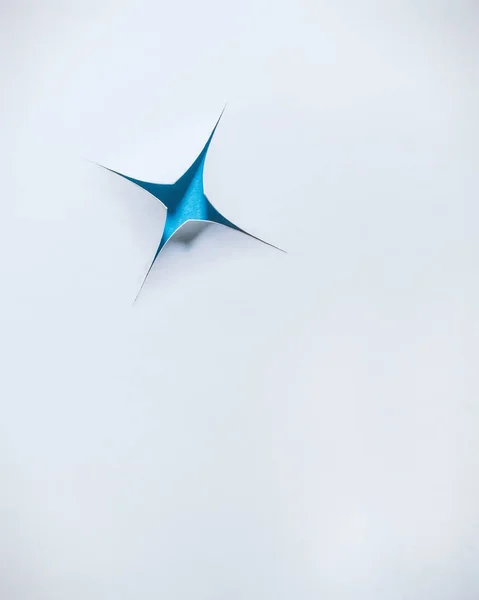 Estrela azul revelada através de um fundo de papel branco brilhante — Fotografia de Stock