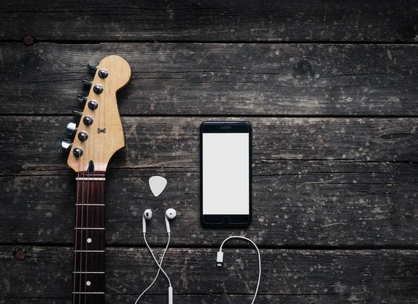White headphones with smartphone and white electric guitar on the old wooden background. Conception: Musician Stuffs on Table.