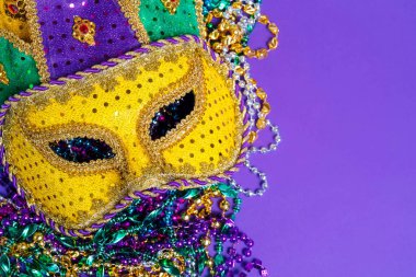 Colorful Mardi Gras or carnival mask on a purple background with beads.