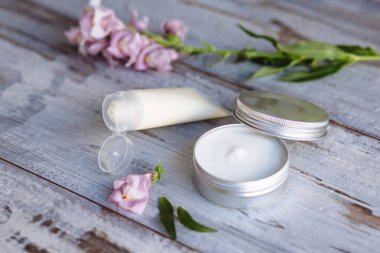Çiçekler arasındaki ahşap arka planda doğal kozmetik kremi ve cilt bakımı. Spa alanında bakım. Yüz serumu ve spa ürünleri.