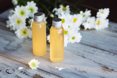 Üst açı, güzellik, cilt bakımı ve sağlık için sıvı içeren küçük şişeyi kapatır. Arka plandaki ahşap masa, iki şişe çiçek ve tatlının bulanık arka planı..