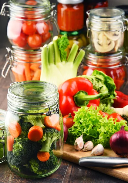 Frascos com alimentos marinados e vegetais crus na tábua de corte — Fotografia de Stock