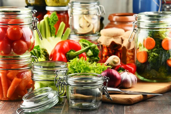 Frascos com alimentos marinados e vegetais crus na tábua de corte — Fotografia de Stock