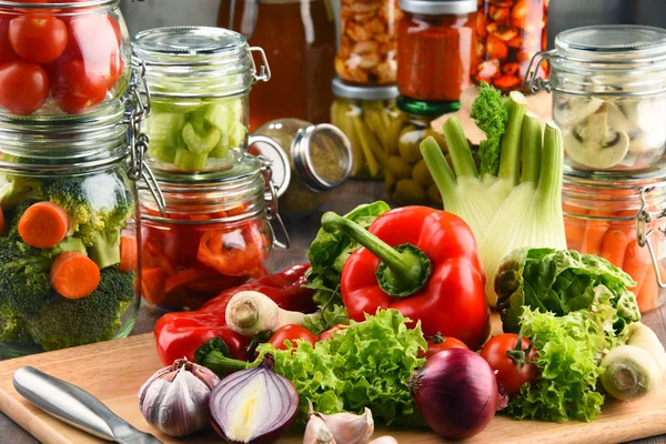 Frascos con comida marinada y verduras crudas en la tabla de cortar —  Fotos de Stock