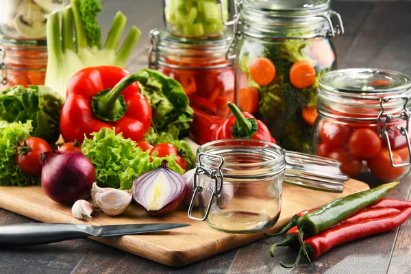 Üvegek, pácolt ételek és a nyers zöldségeket, vágódeszka — Stock Fotó