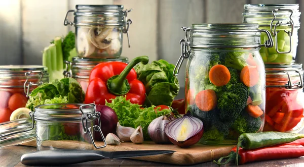 Frascos con comida marinada y verduras crudas en la tabla de cortar —  Fotos de Stock