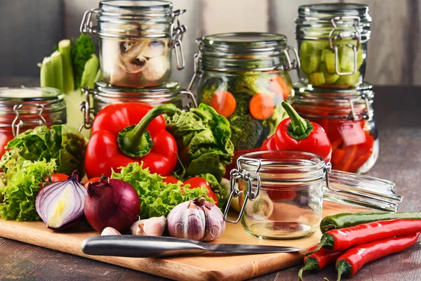 Frascos com alimentos marinados e vegetais crus na tábua de corte — Fotografia de Stock