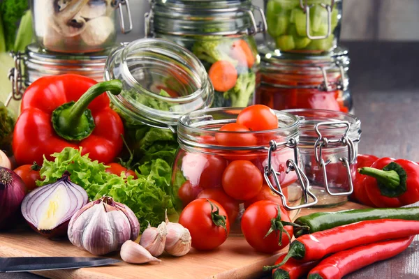 Frascos com alimentos marinados e vegetais crus na tábua de corte — Fotografia de Stock