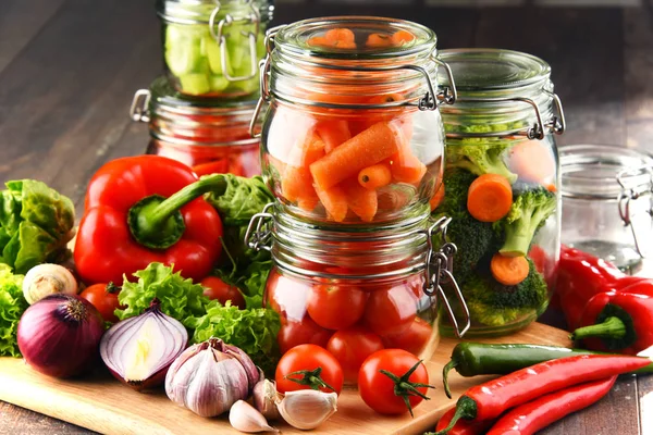 Frascos con comida marinada y verduras crudas en la tabla de cortar —  Fotos de Stock