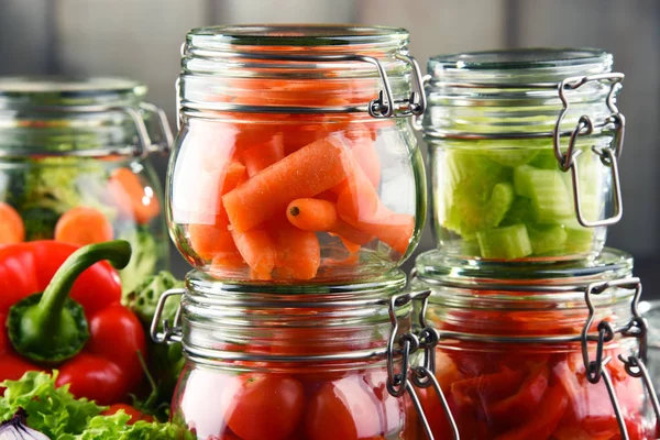 Frascos con comida marinada y verduras crudas en la tabla de cortar — Foto de Stock