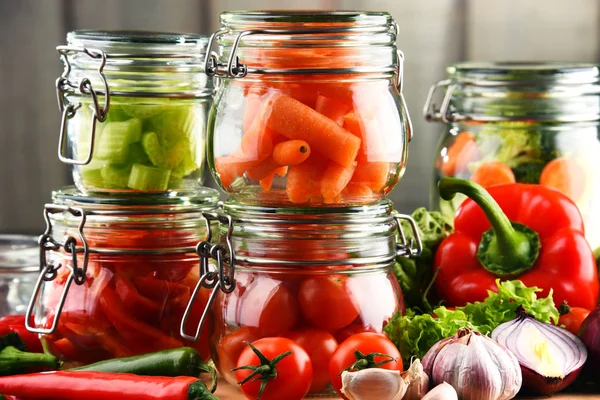Jars with marinated food and raw vegetables on cutting board — Stock Photo, Image