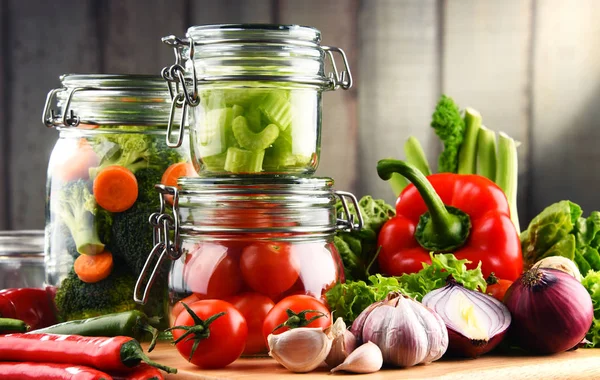 Frascos con comida marinada y verduras crudas en la tabla de cortar — Foto de Stock