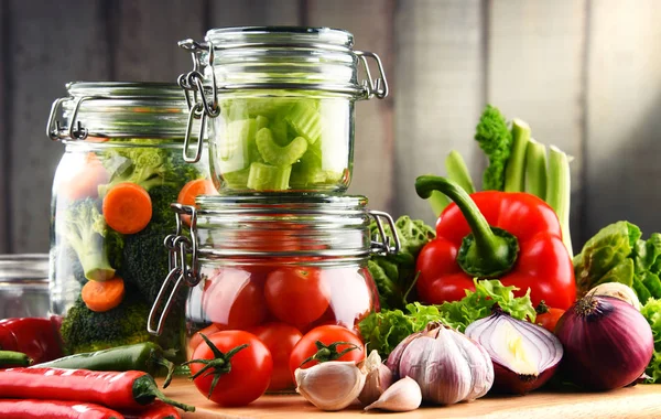 Frascos con comida marinada y verduras crudas en la tabla de cortar —  Fotos de Stock