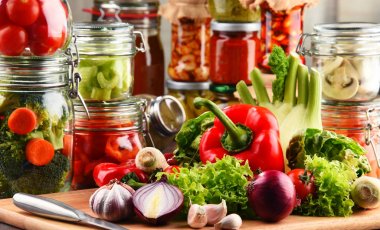 Jars with marinated food and raw vegetables on cutting board clipart