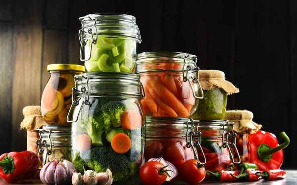 Jars with marinated food and organic raw vegetables — Stock Photo, Image