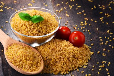 Bowl of uncooked bulgur on wooden table clipart