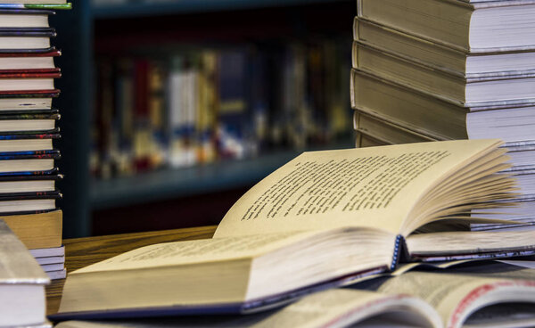 Открытая книга с книгами под и книгами на полках в фоновом режиме
