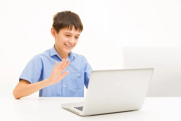 Menino em uma camisa azul usa um laptop sentado em casa a uma mesa — Fotografia de Stock