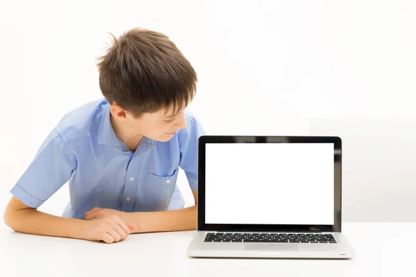 Niño en una camisa azul utiliza un ordenador portátil sentado en el interior de una mesa — Foto de Stock