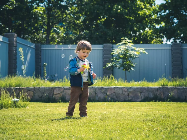 Alegre niño soleado comienza burbujas de jabón de una pistola de juguete. La emoción de la felicidad, la diversión, la alegría del niño. Sonrisa de un niño pequeño y día soleado . — Foto de Stock