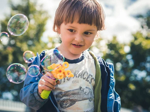 Alegre niño soleado comienza burbujas de jabón de una pistola de juguete. La emoción de la felicidad, la diversión, la alegría del niño. Sonrisa de un niño pequeño y día soleado . — Foto de Stock