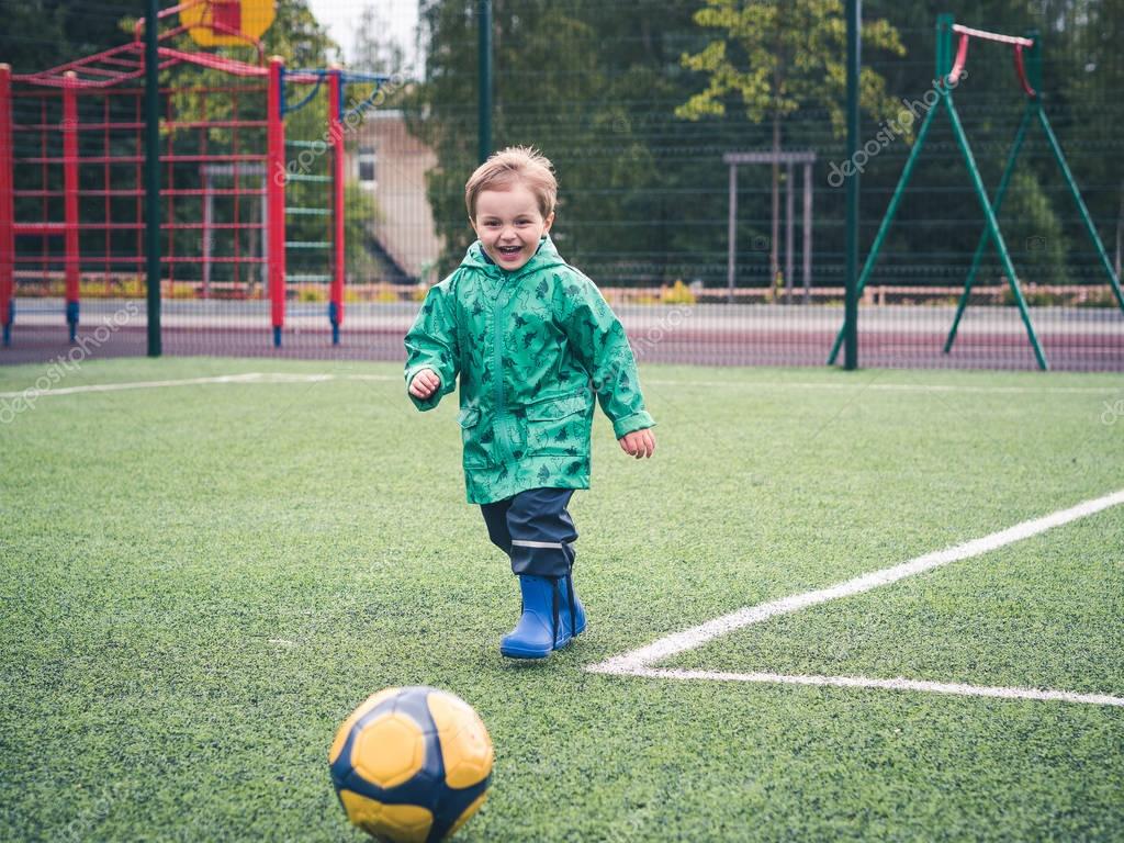 Cute niño pequeño jugando con un balón amarillo en una de los niños en el patio. Deporte, mal ...