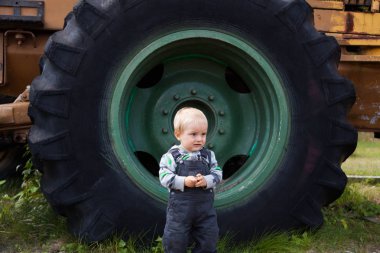 Traktörün büyük bir tekerlek oturan küçük güzel bir çocuk. Ahşap madencilik makine.