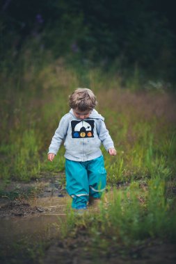 Sevimli kıvırcık bebek bir su birikintisi atlama botlar ve kauçuk pantolon giymiş. Çocukların mutluluğu ile komik çocuk.
