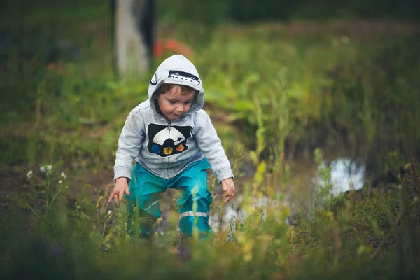 Niedliche lockige Baby in Stiefeln und Gummihosen in einer Pfütze springen gekleidet. Lustiges Kind mit Kinderglück. — Stockfoto