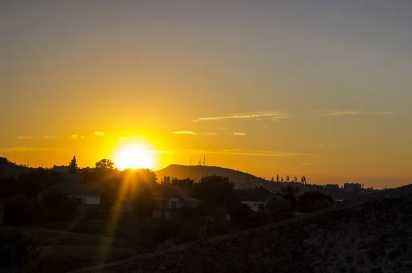 Ein schöner Sonnenuntergang über dem bergigen Gelände, man sieht eine kleine Siedlung und die goldenen Strahlen der Sonne — Stockfoto