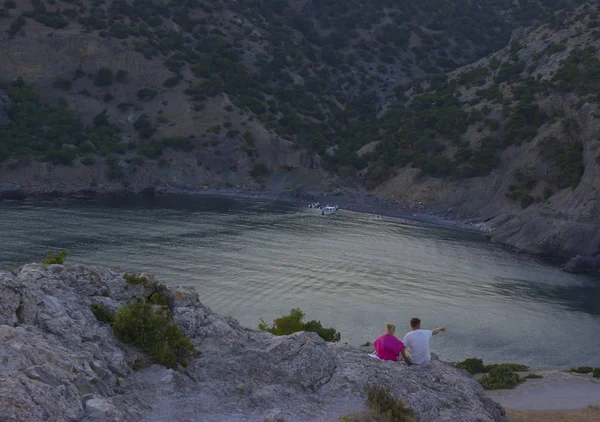 Amoureuze paar zit op een rots en kijkt naar de zee. mooi landschap — Stockfoto