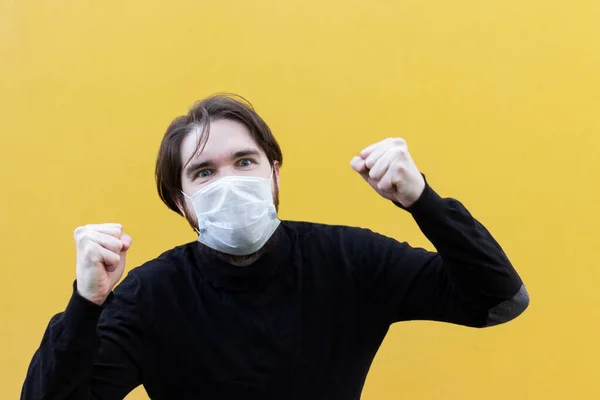 Koronavirüsten korunmak için tek kullanımlık maske takan siyah ceketli bir adam. Sarı arka plan, yüzünde duygular. dağınık erkek saçı. Hastalık durumunda güvenlik önlemleri.