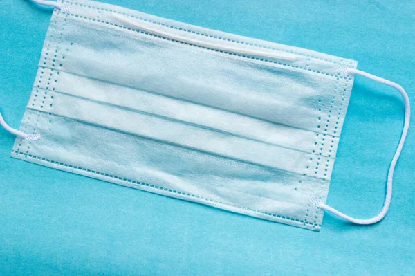 İnsanları tehlikeli bir virüsten korumak için mavi bir tıbbi tek kullanımlık maske 2020 renk eğiliminin arka planında yatıyor. Çin 'de koronavirüs salgını için sağlık ve tıbbi konsept. Termometre yüksek sıcaklık gösteriyor