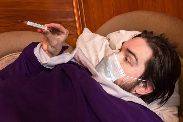 Siyah saçlı ve virüse karşı kendini koruyabilecek tek kullanımlık maskeli bir adam evde yatıp kendini diğer insanlardan soyutluyor. Ateş, baş ağrısı ve bulantı belirtilerdir - sağlığınıza dikkat edin