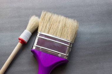 Güzel gri bir arka planda çiti boyamak için büyük ve küçük fırçalar. Bahar geldi, köyde çalışma zamanı. Boyaları ve inşaatı tanıtmak için kullanabiliriz.