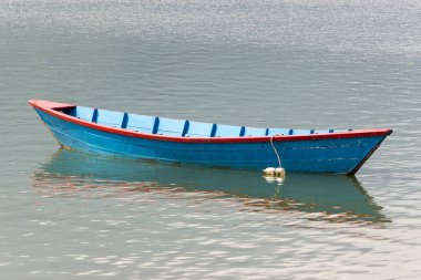 Suyun şeffaf ve güzel bir yüzeyinde mavi bir tekne. Turistik tatil beldesinde turist bulunmuyor. Sınırlar koronavirüs nedeniyle kapalı ve ticarete zarar veren turist sayısı azalıyor.