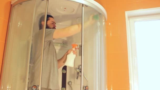 コロナウイルス中の家の安全のためのシャワーキャビンを衛生的に掃除する灰色のTシャツとひげの男は バスルームを消毒します — ストック動画