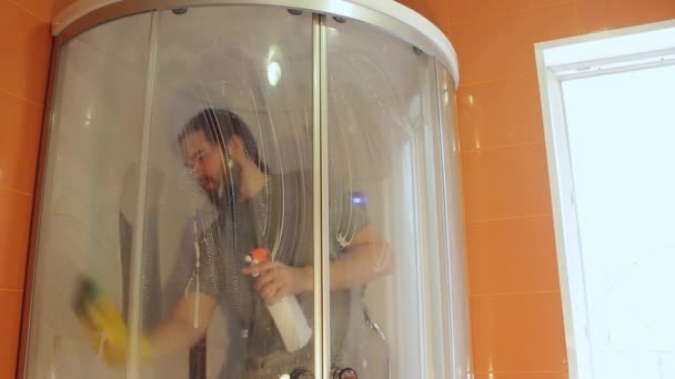 コロナウイルス中の家の安全のためのシャワーキャビンを衛生的に掃除する灰色のTシャツとひげの男は バスルームを消毒します — ストック動画