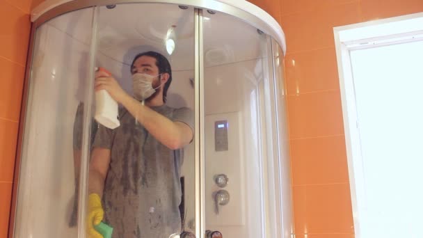 コロナウイルス中の家の安全のためのシャワーキャビンの衛生的な清掃灰色のTシャツとひげの男は 使い捨てのマスクを着て バスルームを消毒します — ストック動画