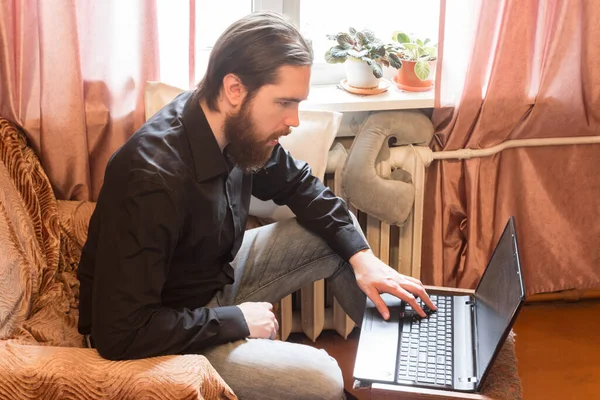 self-isolation mode in the world due to the coronavirus problem.a man with dark hair and a thick beard, works at home as a self-employed remote worker.laptop and phone, bad emotions of anger and fear