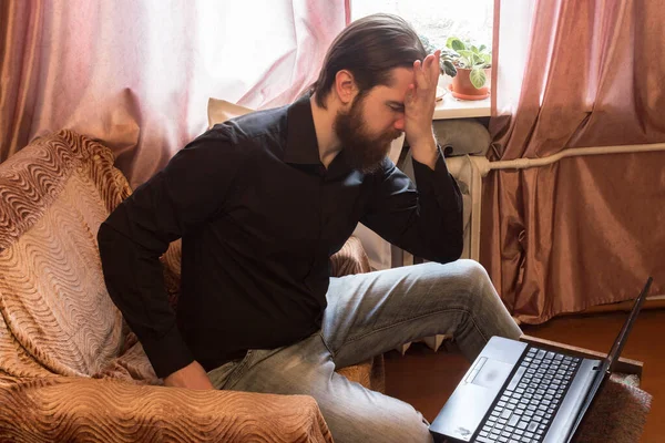 self-isolation mode in the world due to the coronavirus problem.a man with dark hair and a thick beard, works at home as a self-employed remote worker.laptop and phone, bad emotions of anger and fear