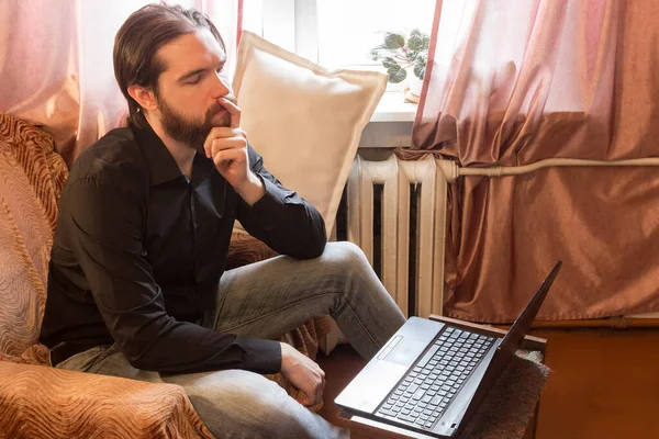 self-isolation mode in the world due to the coronavirus problem.a man with dark hair and a thick beard, works at home as a self-employed remote worker.laptop and phone, bad emotions of anger and fear