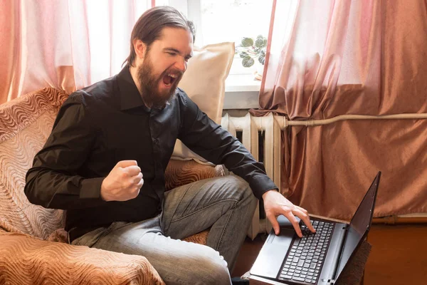 self-isolation mode in the world due to the coronavirus problem.a man with dark hair and a thick beard, works at home as a self-employed remote worker.laptop and phone, bad emotions of anger and fear