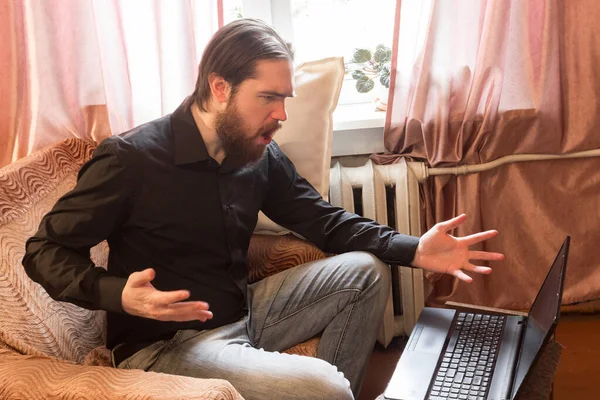 self-isolation mode in the world due to the coronavirus problem.a man with dark hair and a thick beard, works at home as a self-employed remote worker.laptop and phone, bad emotions of anger and fear