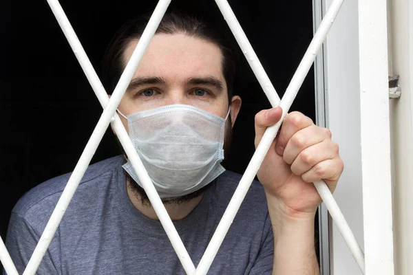 male model in a disposable mask, dark hair, beard and grey t-shirt.A coronavirus patient remains at home under quarantine and disease prevention.Sad and negative Emotions in the eyes of a person