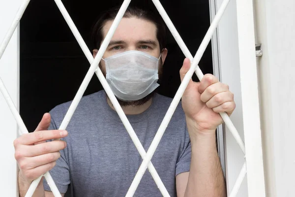 male model in a disposable mask, dark hair, beard and grey t-shirt.A coronavirus patient remains at home under quarantine and disease prevention.Sad and negative Emotions in the eyes of a person