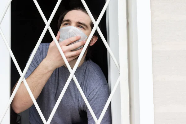 male model in a disposable mask, dark hair, beard and grey t-shirt.A coronavirus patient remains at home under quarantine and disease prevention.Sad and negative Emotions in the eyes of a person