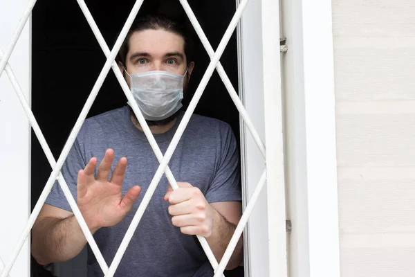 Tek kullanımlık maskeli, siyah saçlı, sakallı ve gri tişörtlü bir erkek manken. Coronavirus hastası evde karantina ve hastalık önleme altında kalıyor. Bir insanın gözlerinde olumsuz ve olumsuz duygular